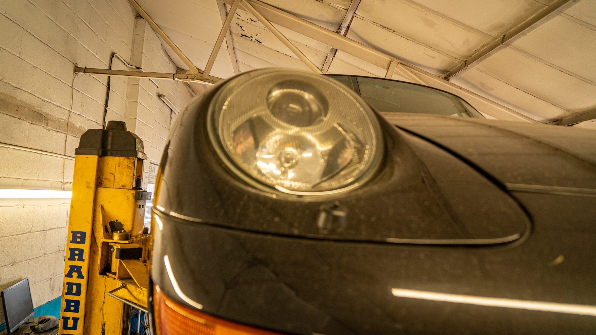 Porsche 911 headlight beside a vehicle lift in the workshop