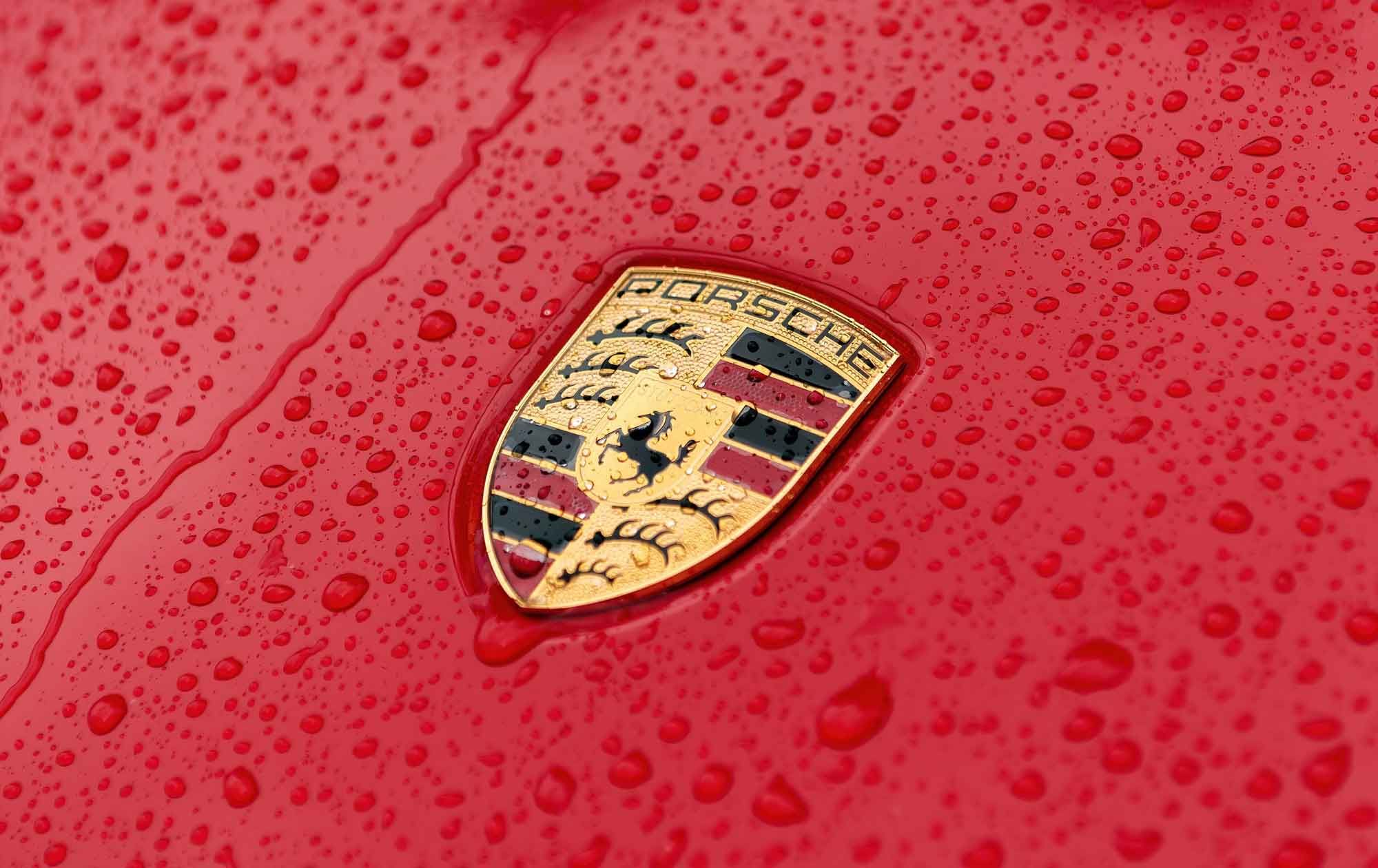 Porsche crest on a red bonnet covered in raindrops