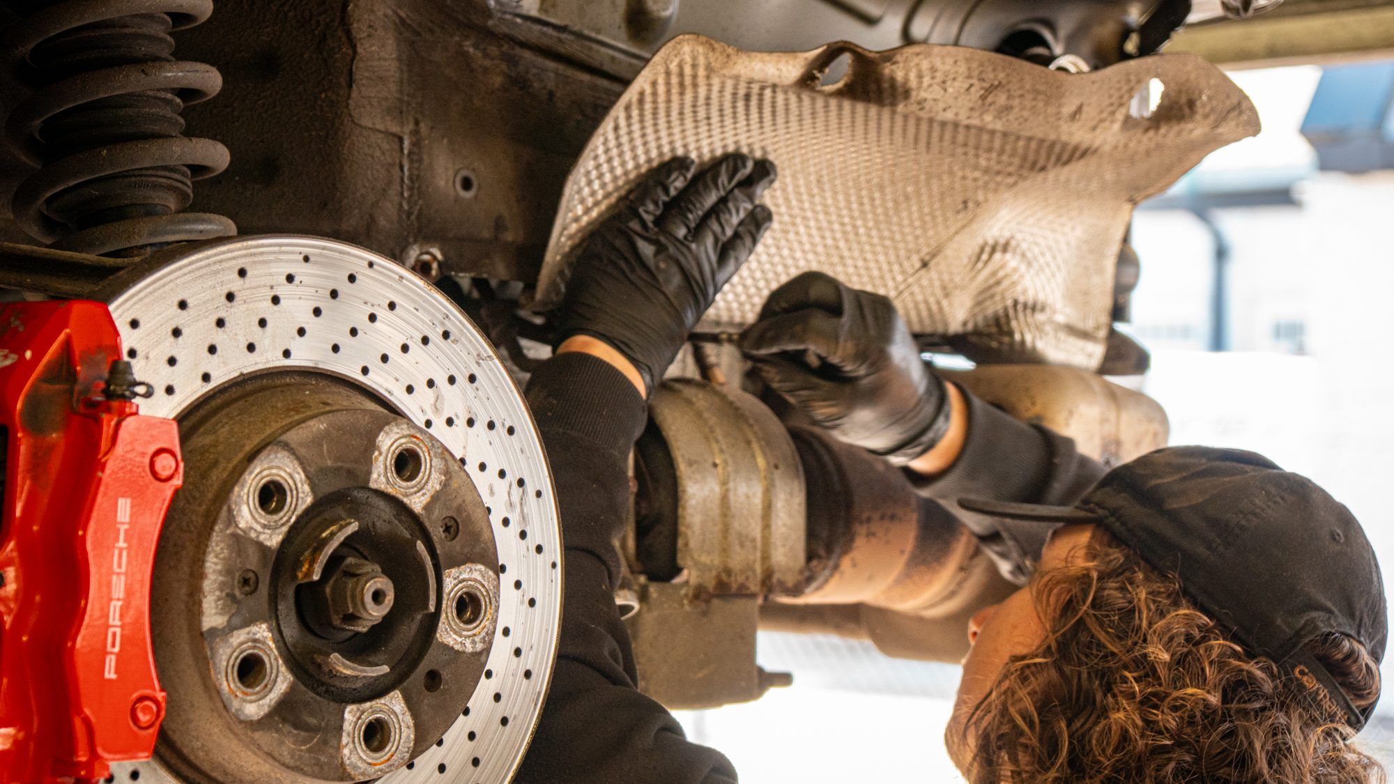 Technician working under a Porsche with red brake calipers