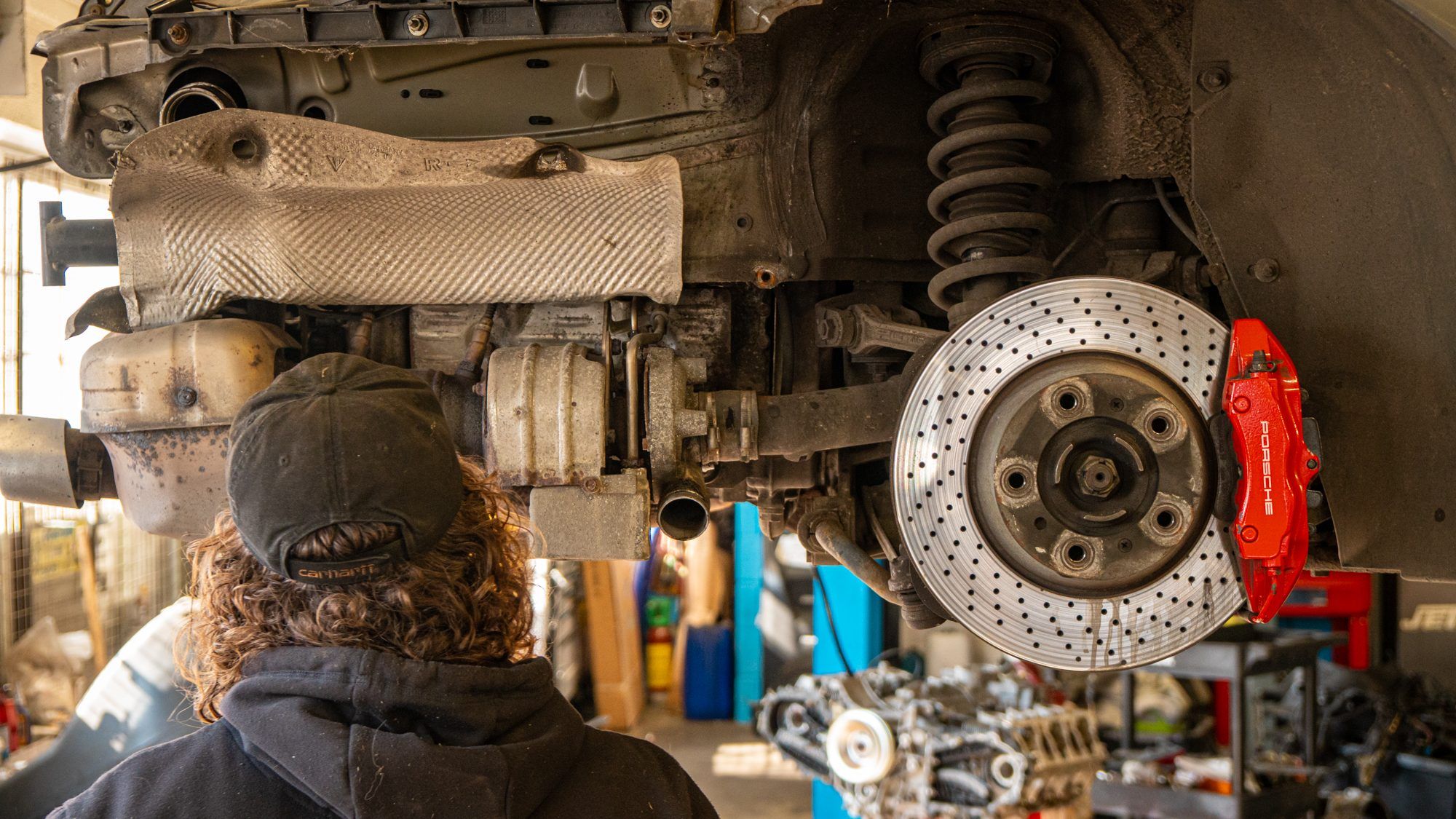 Technician inspecting a Porsche on a lift, with red brake calipers